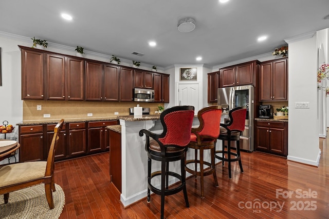 kitchen featuring a kitchen breakfast bar, dark wood-type flooring, a center island, stainless steel appliances, and stone counters