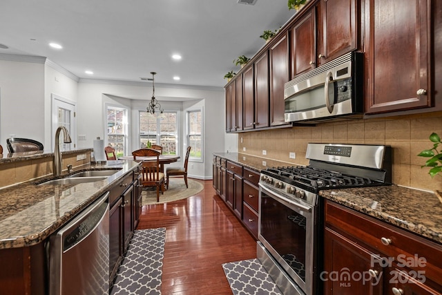 kitchen with appliances with stainless steel finishes, dark stone counters, decorative light fixtures, and a sink