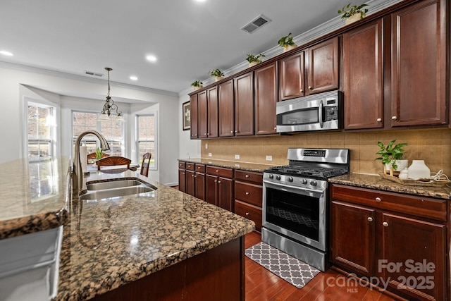 kitchen featuring dark stone counters, ornamental molding, decorative light fixtures, stainless steel appliances, and a sink