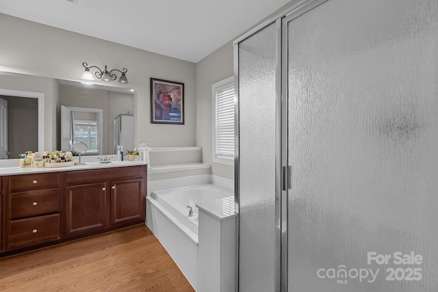 full bath with wood finished floors, vanity, a healthy amount of sunlight, a bath, and a stall shower