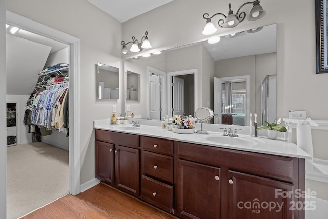 ensuite bathroom with double vanity, wood finished floors, a sink, and a walk in closet