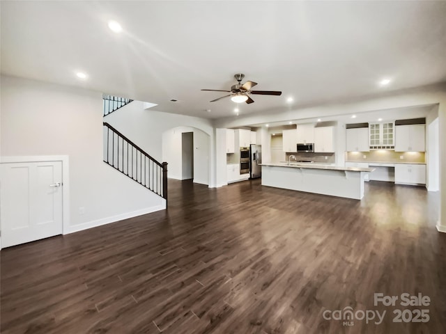 unfurnished living room with stairs, arched walkways, dark wood finished floors, and recessed lighting