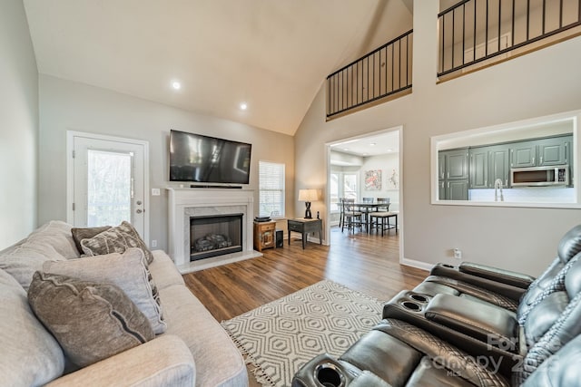 living area with wood finished floors, baseboards, high vaulted ceiling, a fireplace, and recessed lighting