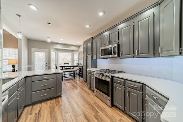 kitchen featuring pendant lighting, light wood-type flooring, light countertops, decorative backsplash, and stainless steel appliances