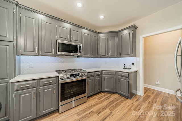 kitchen with appliances with stainless steel finishes, light wood-type flooring, light countertops, and gray cabinetry