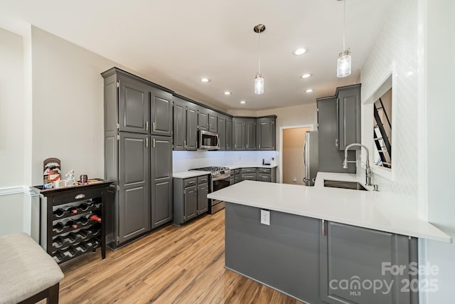 kitchen with gray cabinetry, a sink, stainless steel appliances, a peninsula, and light wood finished floors