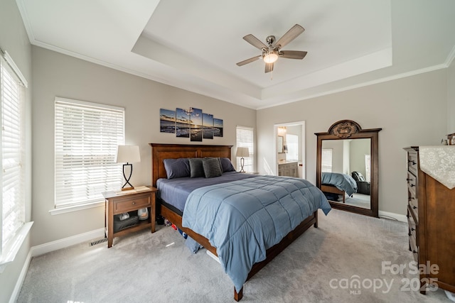 bedroom featuring ensuite bath, a tray ceiling, baseboards, and light carpet