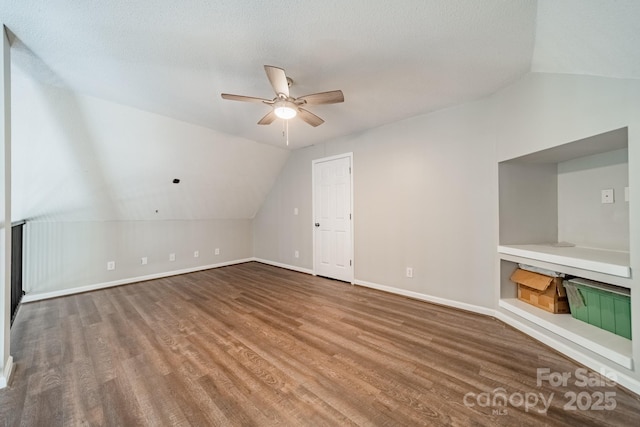 additional living space featuring baseboards, ceiling fan, vaulted ceiling, wood finished floors, and a textured ceiling