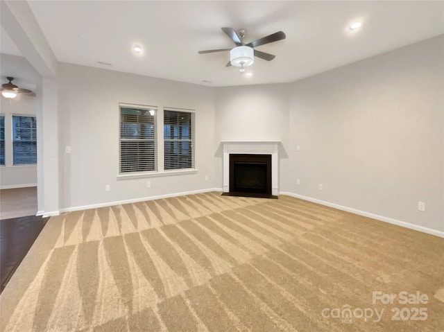 unfurnished living room with a ceiling fan, a fireplace with flush hearth, baseboards, and carpet flooring