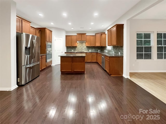 kitchen featuring dark wood-style flooring, appliances with stainless steel finishes, tasteful backsplash, brown cabinetry, and dark countertops