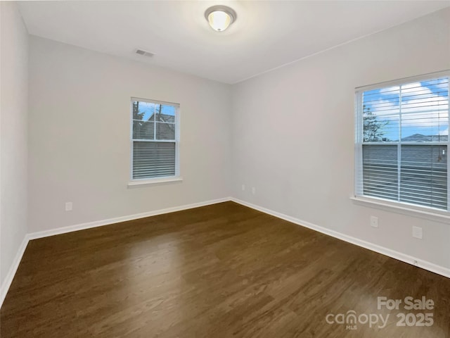 empty room featuring dark wood-style floors, visible vents, and baseboards