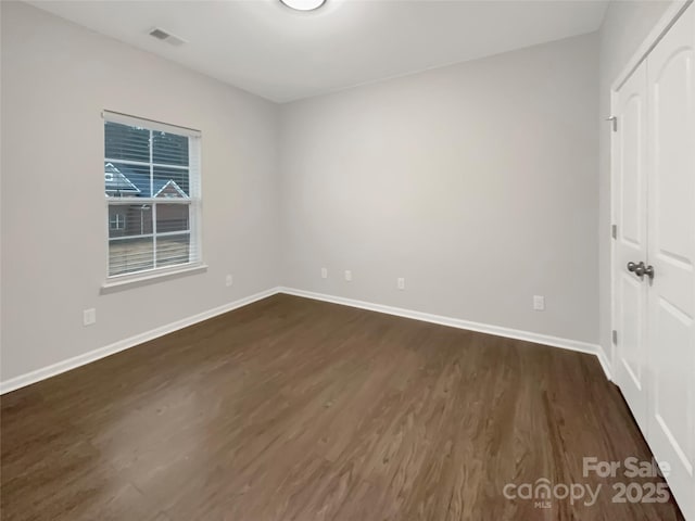 unfurnished room featuring dark wood-style floors, visible vents, and baseboards