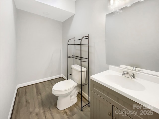 half bath featuring baseboards, vanity, toilet, and wood finished floors