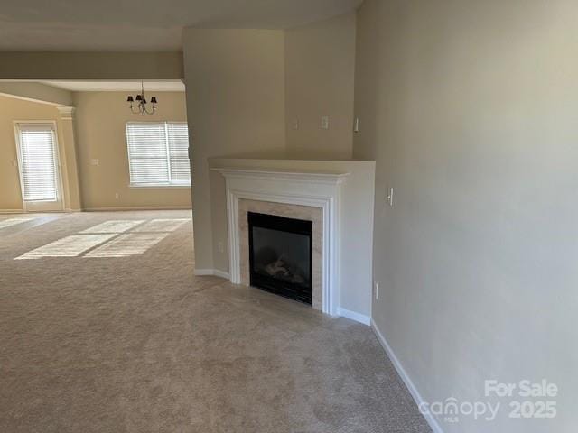 unfurnished living room featuring a chandelier, a glass covered fireplace, carpet flooring, and baseboards