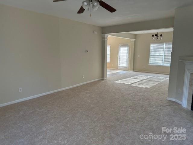 unfurnished room featuring light carpet, ceiling fan with notable chandelier, a fireplace, and baseboards