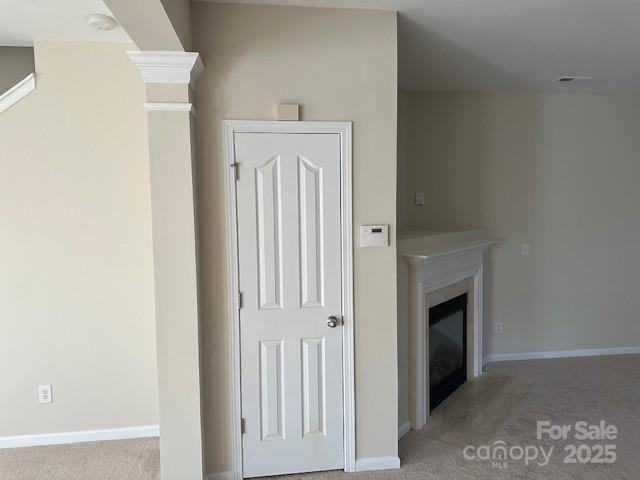 interior space with ornate columns, baseboards, light colored carpet, and a glass covered fireplace