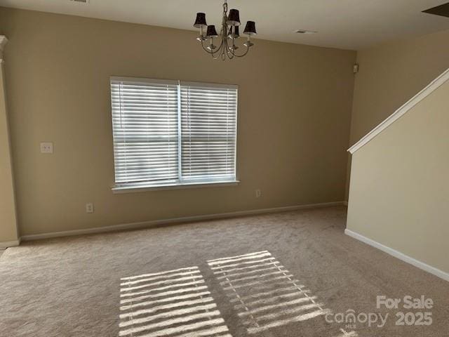 empty room featuring light carpet, baseboards, and a notable chandelier