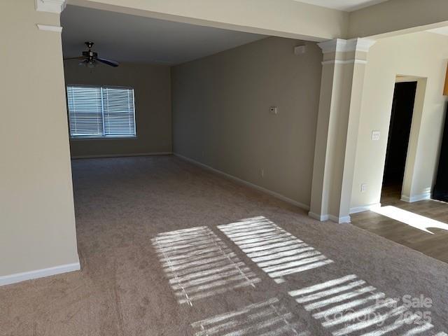 carpeted spare room featuring a ceiling fan, baseboards, and ornate columns