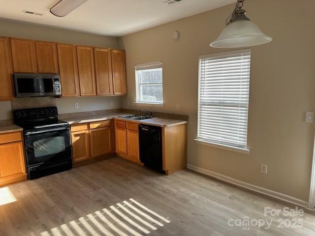 kitchen with black appliances, pendant lighting, light countertops, and a sink