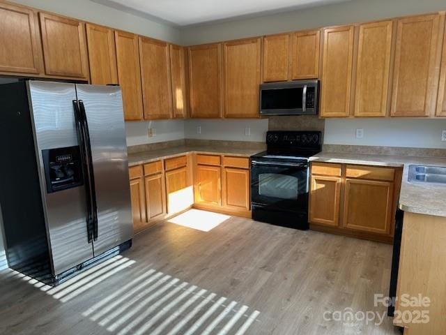 kitchen featuring black electric range, light countertops, light wood-style flooring, a sink, and stainless steel fridge