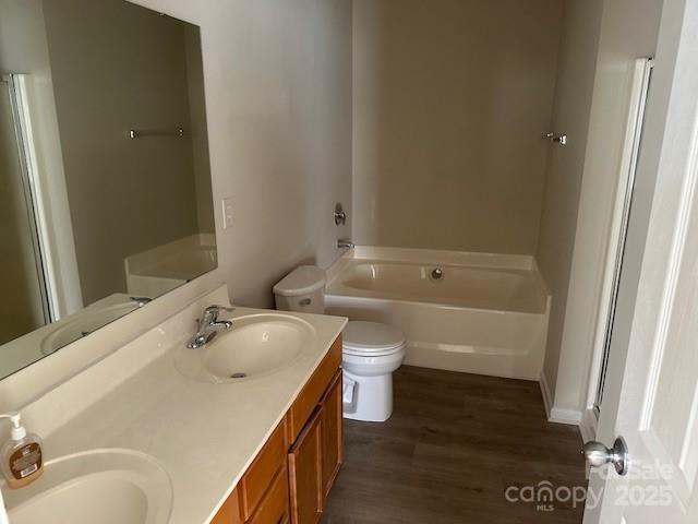 full bath featuring wood finished floors, a garden tub, a sink, and double vanity