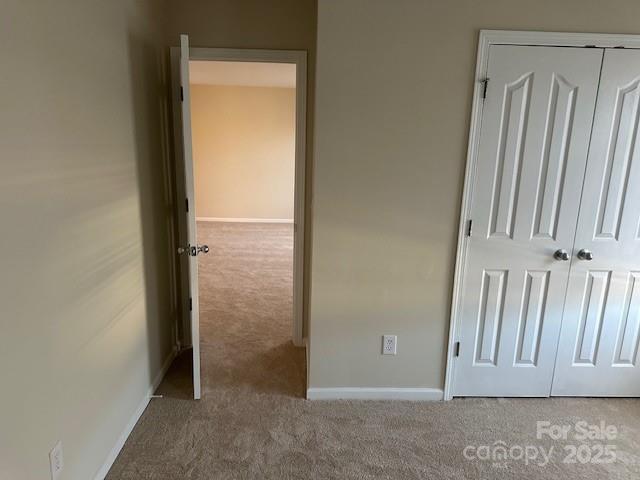 unfurnished bedroom with a closet, light colored carpet, and baseboards