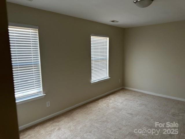 spare room featuring light carpet, visible vents, a wealth of natural light, and baseboards