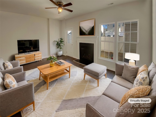 living area with a fireplace, visible vents, a ceiling fan, wood finished floors, and baseboards