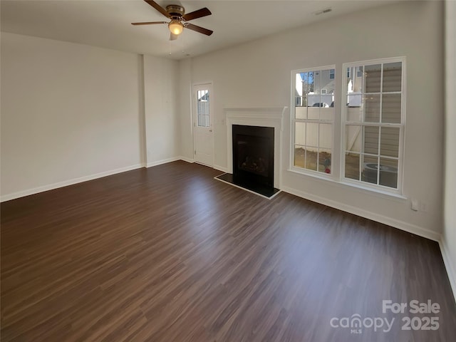 unfurnished living room with dark wood-style floors, visible vents, a fireplace with raised hearth, ceiling fan, and baseboards