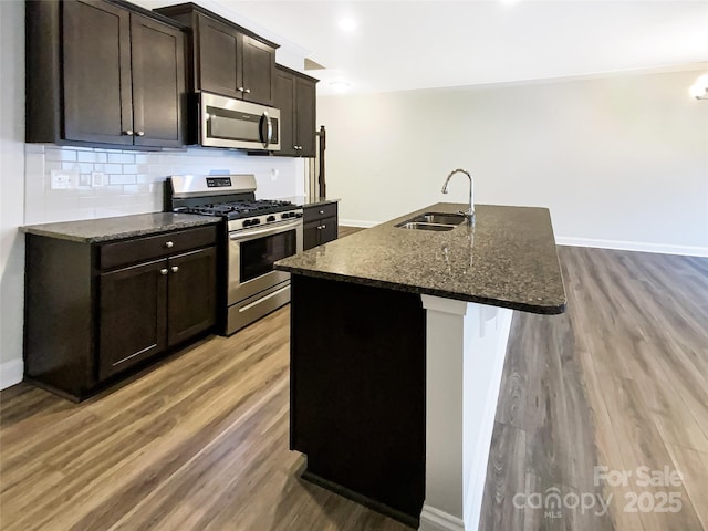 kitchen with appliances with stainless steel finishes, light wood-type flooring, a sink, and dark stone countertops