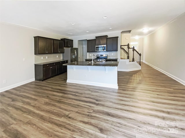 kitchen with a breakfast bar, dark countertops, appliances with stainless steel finishes, a sink, and wood finished floors