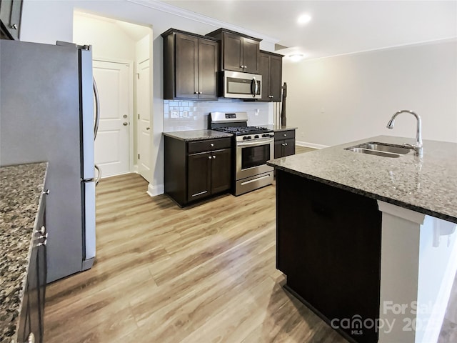 kitchen with tasteful backsplash, light wood-style flooring, stainless steel appliances, stone counters, and a sink