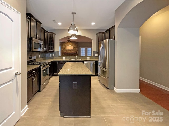 kitchen featuring arched walkways, a kitchen island, appliances with stainless steel finishes, backsplash, and decorative light fixtures