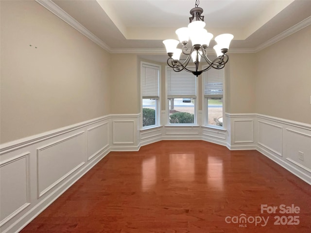 unfurnished dining area with a tray ceiling, a notable chandelier, a decorative wall, and wood finished floors