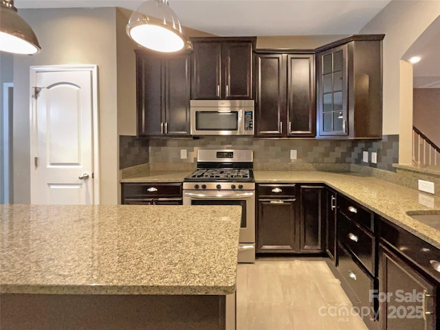 kitchen featuring glass insert cabinets, dark brown cabinetry, appliances with stainless steel finishes, and backsplash