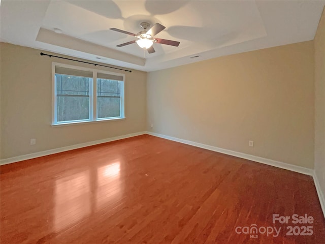 unfurnished room featuring ceiling fan, baseboards, a raised ceiling, and wood finished floors