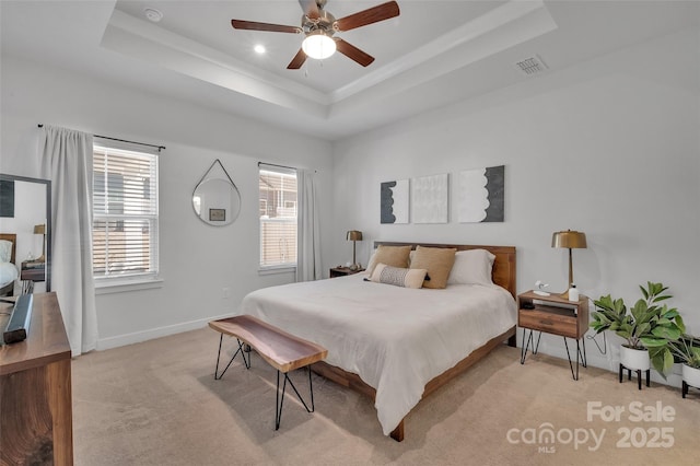 bedroom with a tray ceiling, light colored carpet, visible vents, a ceiling fan, and baseboards