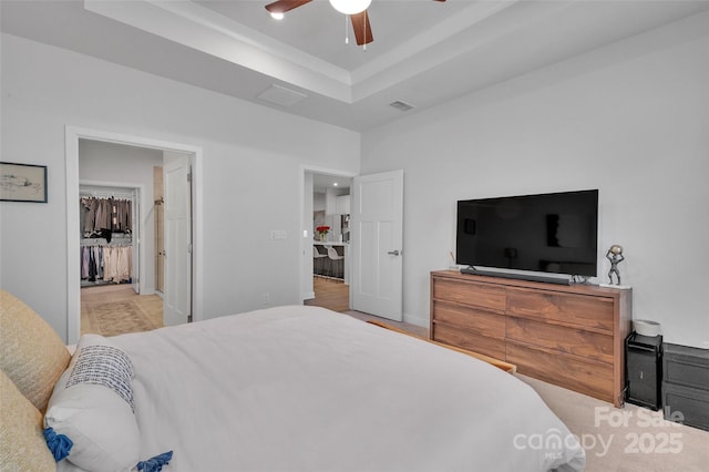 bedroom with a ceiling fan, a tray ceiling, visible vents, and a spacious closet
