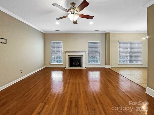 unfurnished living room featuring a fireplace with flush hearth, ornamental molding, a wealth of natural light, and wood finished floors