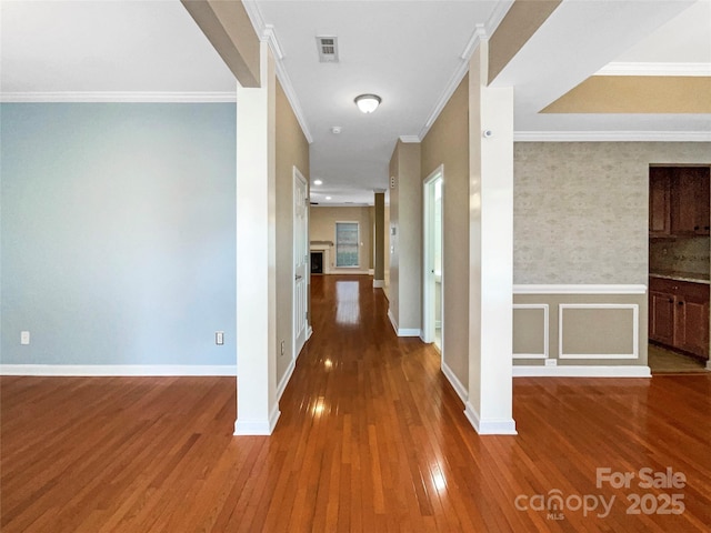 hall featuring visible vents, baseboards, wainscoting, wood-type flooring, and ornamental molding