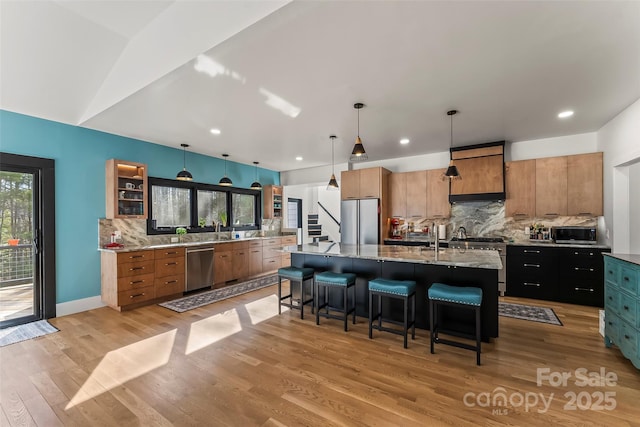 kitchen with light wood finished floors, a large island, stainless steel appliances, a kitchen bar, and backsplash