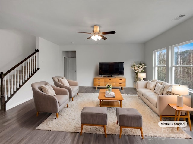 living room featuring stairs, visible vents, baseboards, and wood finished floors