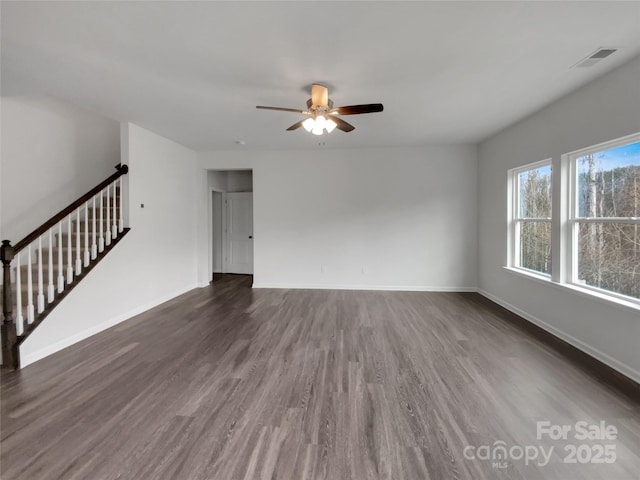 empty room featuring baseboards, visible vents, a ceiling fan, dark wood-type flooring, and stairs