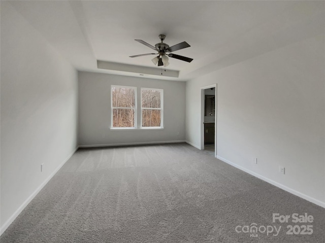 unfurnished bedroom featuring light carpet, baseboards, a tray ceiling, and a ceiling fan