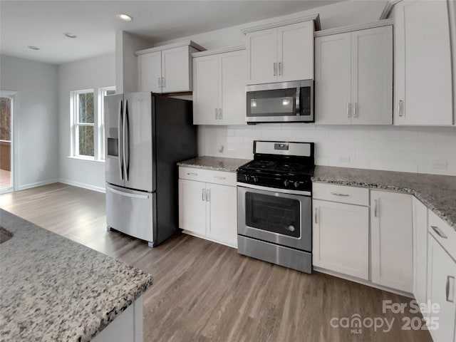 kitchen featuring appliances with stainless steel finishes, backsplash, light stone countertops, and white cabinets