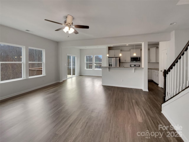 unfurnished living room featuring ceiling fan, dark wood finished floors, baseboards, and stairs