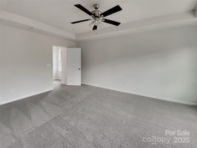 carpeted empty room featuring ceiling fan, a raised ceiling, and baseboards