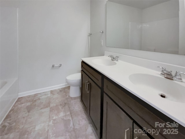 full bath featuring double vanity, a sink, toilet, and baseboards