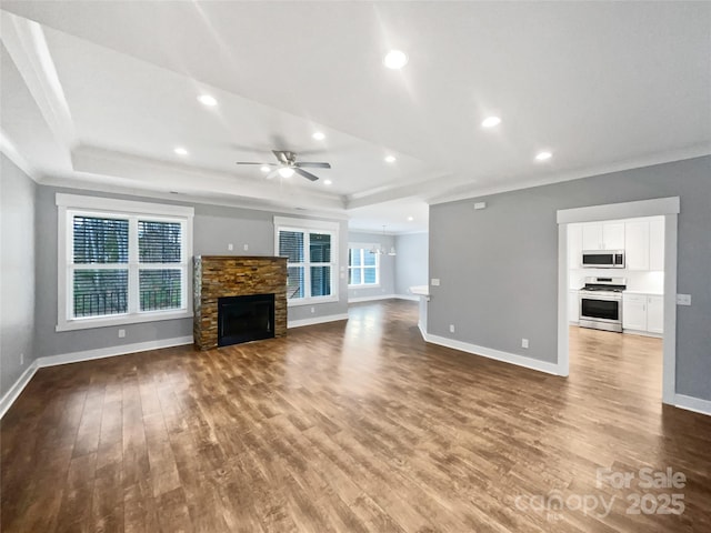 unfurnished living room featuring a raised ceiling, a stone fireplace, baseboards, and wood finished floors