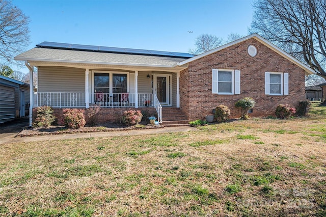 ranch-style house featuring covered porch, brick siding, a front lawn, and solar panels